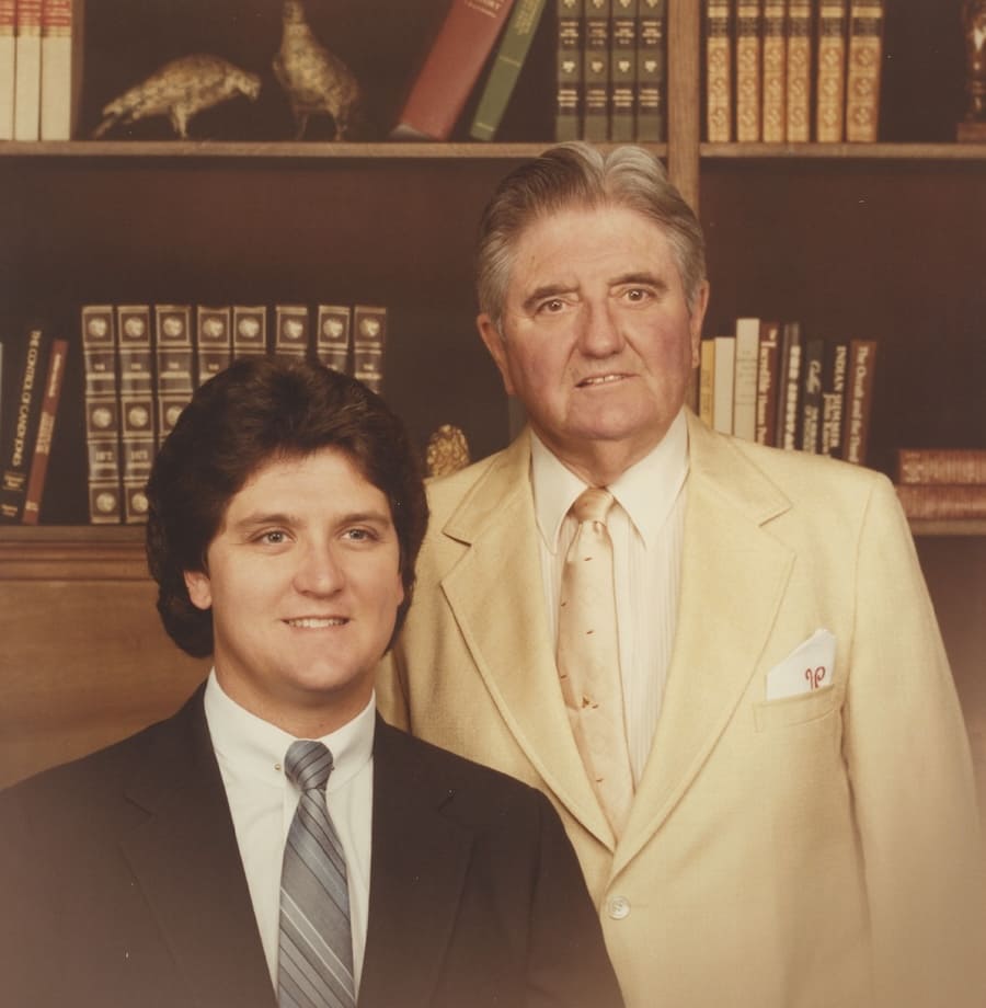 Two men in suits posing for a formal portrait in front of a wooden bookcase.