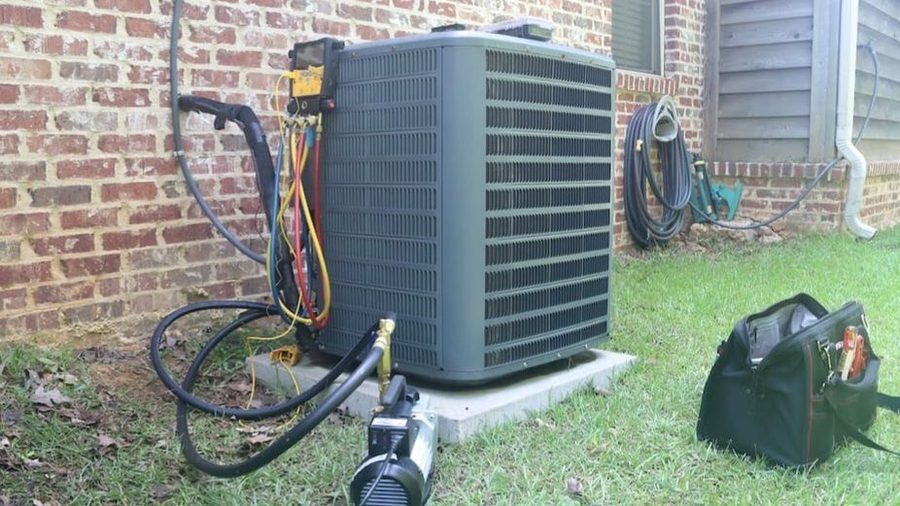 Outdoor HVAC condenser unit with service gauges attached during air conditioning maintenance beside a residential home.