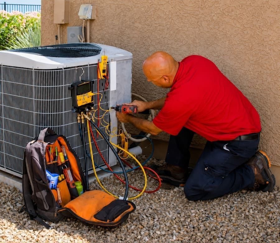 HVAC technician kneels beside an outdoor AC condenser, working with wires and diagnostic tools.