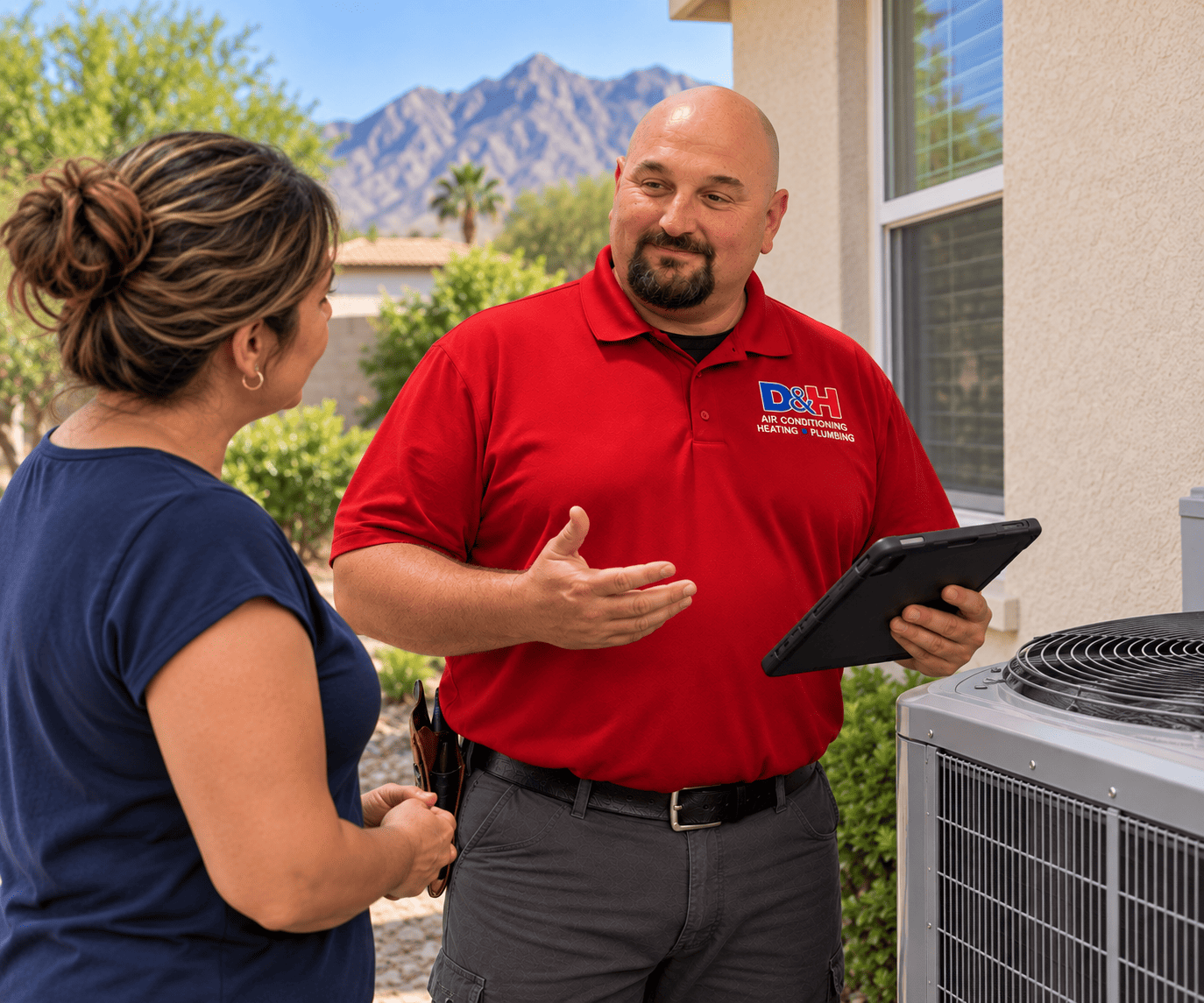 HVAC technician in a red polo explains an outdoor air conditioner to a homeowner, tablet in hand outside a house.